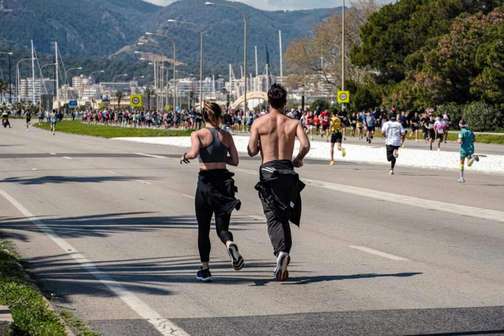 Beginner’s Guide to Running: How to Start, What to Expect, and How to Keep Going "A diverse male and female runner in athletic gear smiling while competing together in a crowded street marathon, representing inclusive fitness and beginner running motivation."